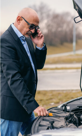 Man on cell phone looking under the hood of his car