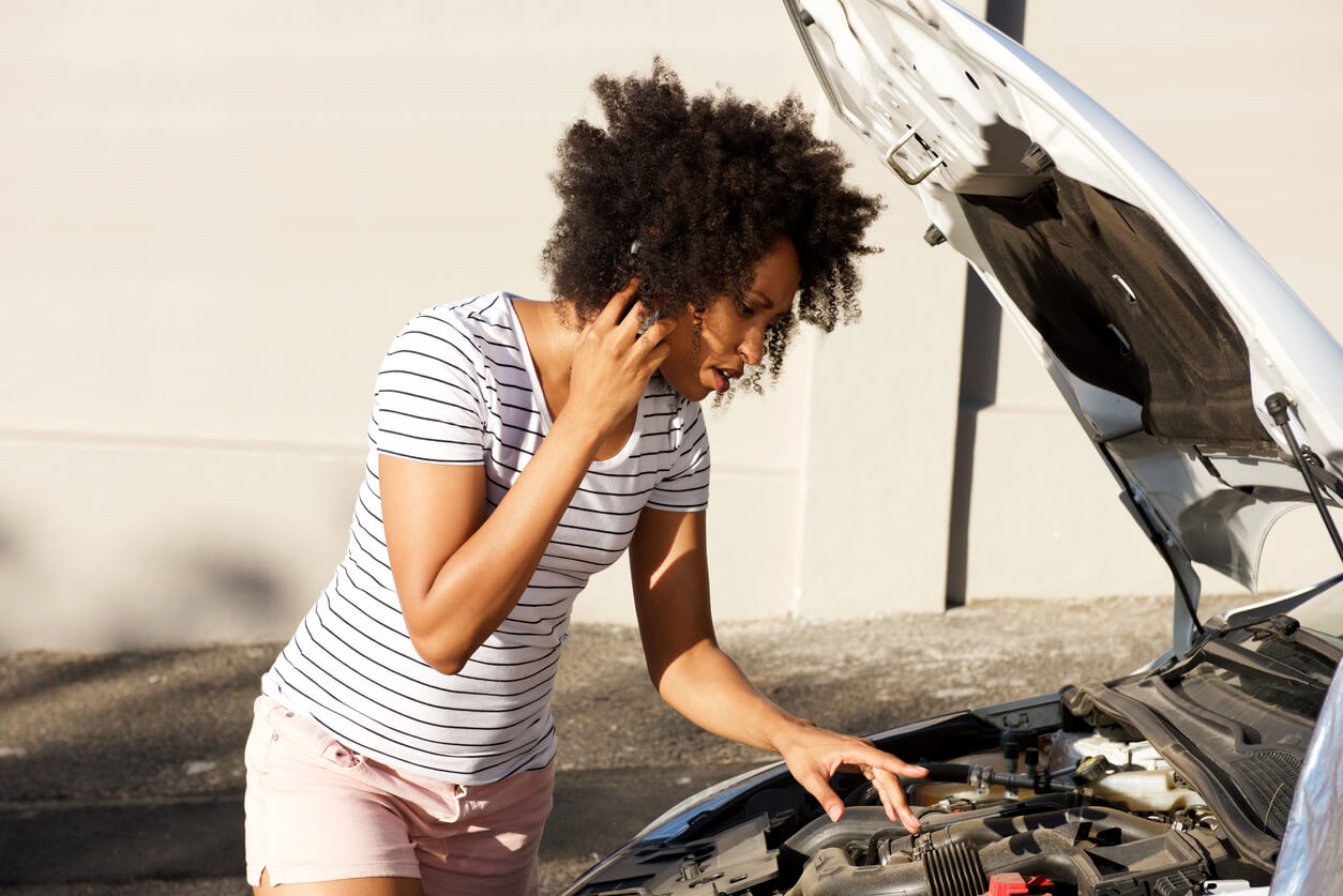 African American woman checking the hood of her car.